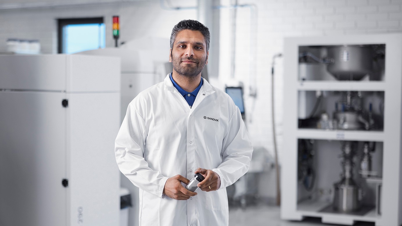 Dr. Faraz Deirmina holding a powder sample in a glass jar.